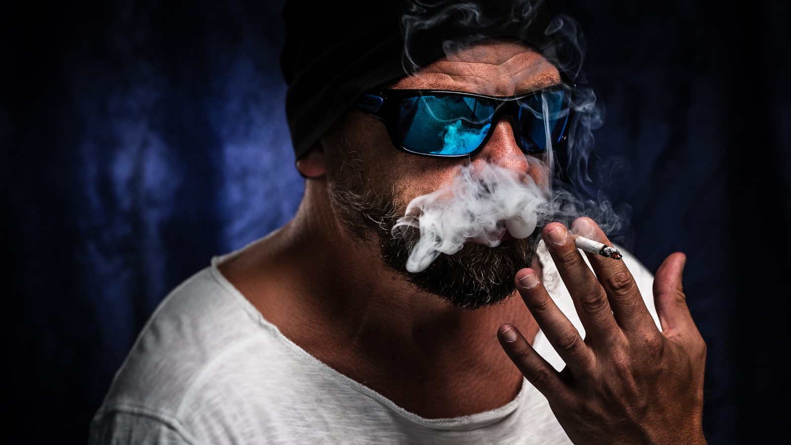 Homem com óculos escuros fumando em um quarto escuro Por wirestock