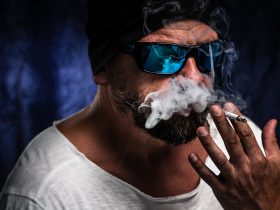 Homem com óculos escuros fumando em um quarto escuro Por wirestock