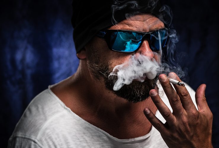 Homem com óculos escuros fumando em um quarto escuro Por wirestock