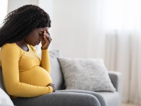 Jovem mulher negra grávida com dor de cabeça ou enxaqueca Por Prostock-studio