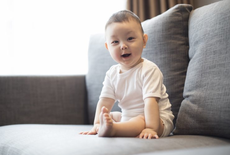 Menino fofo sentado no sofá Por bluejeanimages