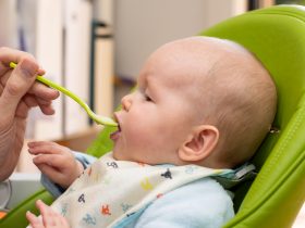 Alimentando o bebê com uma colher cheia de mingau de arroz para bebês. Primeiros sólidos do bebê. Desmame. Por Daria_Nipot