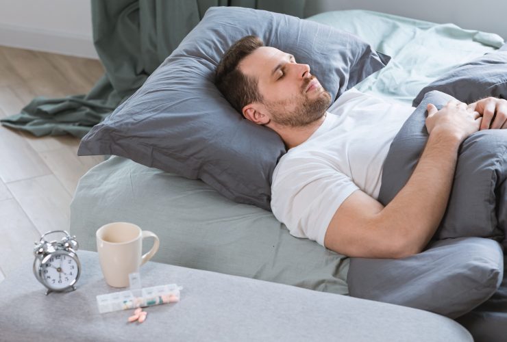 Homem dorme na cama depois de tomar pílulas para dormir no quarto Por Prostock-studio