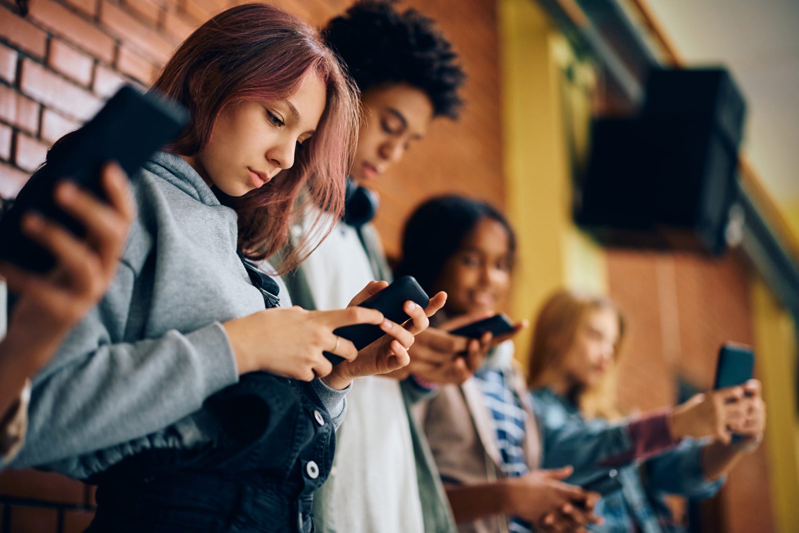 Grupo de adolescentes usando telefones celulares no corredor do ensino médio. Por drazenphoto