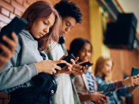 Grupo de adolescentes usando telefones celulares no corredor do ensino médio. Por drazenphoto