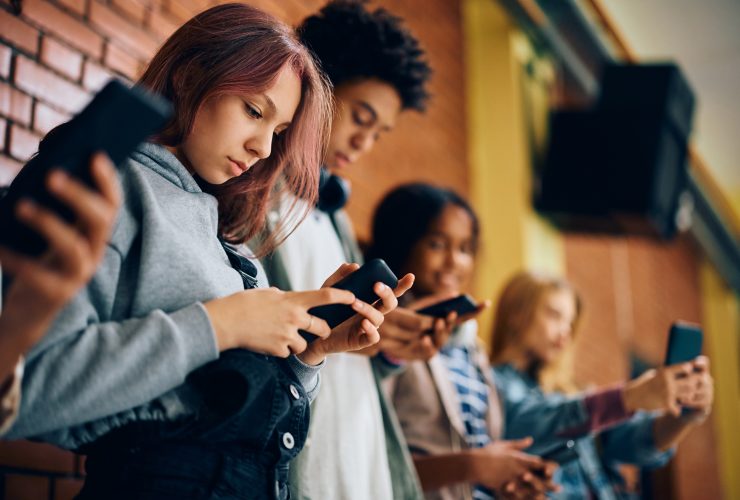 Grupo de adolescentes usando telefones celulares no corredor do ensino médio. Por drazenphoto