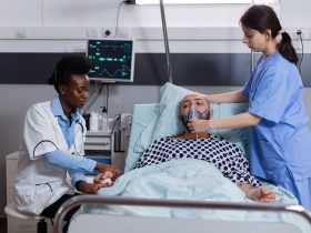 Paciente doente deitado na cama enquanto enfermeira coloca máscara de oxigênio Por DC_Studio