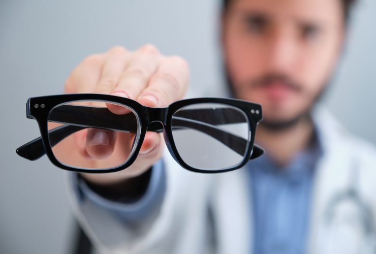 Médico irreconhecível sugerindo óculos para uma pessoa com problemas de visão. Por Ladanifer