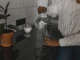 Mulher afro-americana sedenta de perto bebendo água mineral na cozinha, derramando líquido saudável Por Satura_