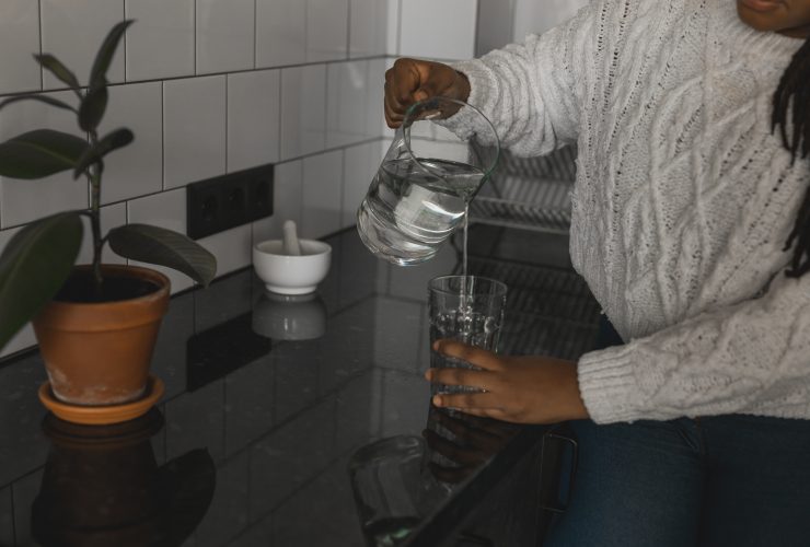 Mulher afro-americana sedenta de perto bebendo água mineral na cozinha, derramando líquido saudável Por Satura_