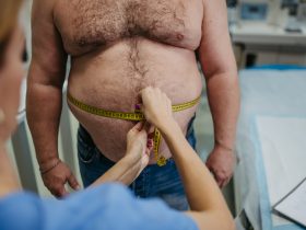 Médica medindo a cintura de um paciente com sobrepeso usando fita métrica. Obesidade afetando o meio Por halfpoint