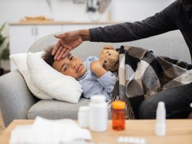 Pai verificando a temperatura da criança doente no sofá Por sofiiashunkina