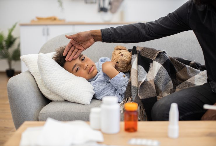 Pai verificando a temperatura da criança doente no sofá Por sofiiashunkina