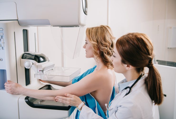 jovem radiologista em pé perto do paciente enquanto fazia o teste de mamografia na máquina de raio-x Por LightFieldStudios