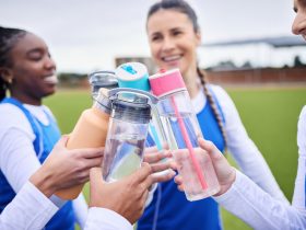 Grupo de mulheres esportivas, grama e garrafa em círculo para brinde, celebração e diversidade com formação de equipe Por YuriArcursPeopleimages