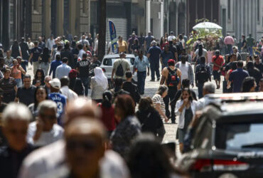 Imagem de pessoas andando em avenida movimentada.